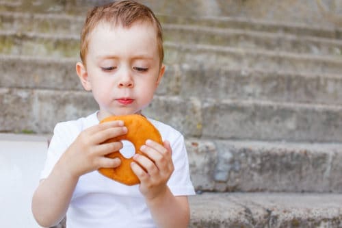 kid sitting on the steps with a donut in hands. little boy is looking forward to eating a donut. copy space for your text