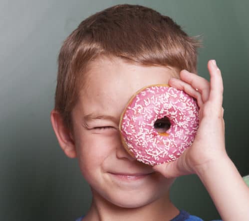 Grundschüler vor Tafel schaut durch seinen Donut